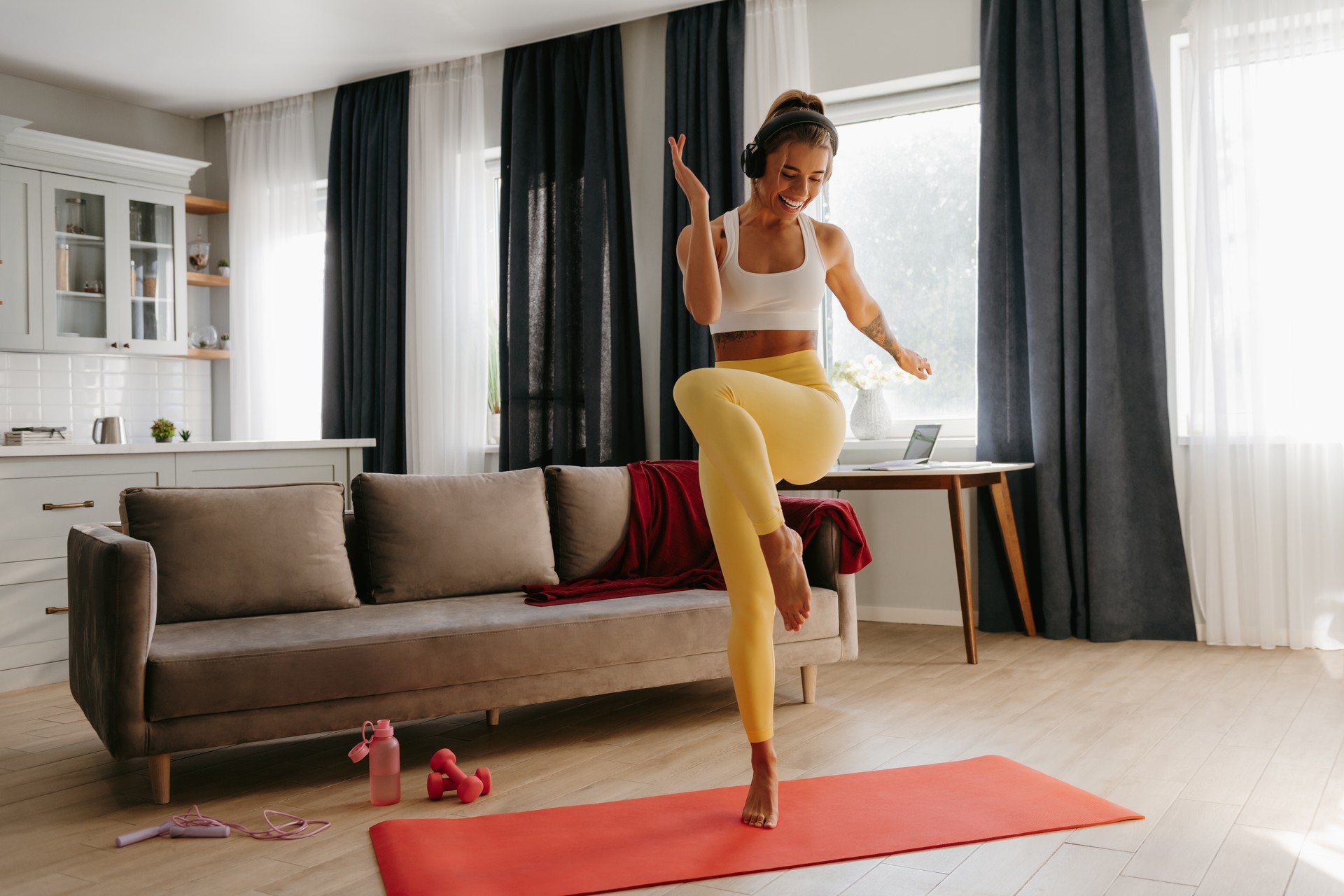 Full length of smiling young sporty woman in headphones doing aerobics while training at home